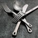 Oneida Cooper stainless steel soup ladle on a table with a fork, spoon, and knife.