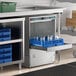 An undercounter high temperature dishwashing machine with a blue rack holding glassware.