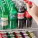 A hand pushing a soda bottle into a green Avantco bottle lane organizer.