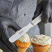 A person using an Ateco straight blade spatula to frost a cupcake.