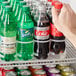 A hand using an Avantco 10 lane gravity feed bottle organizer to get a soda bottle.