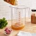 A person pouring brown liquid into a Choice clear plastic measuring cup on a kitchen counter.