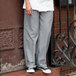 A person in Uncommon Chef houndstooth chef pants and sneakers stands on a step in a professional kitchen.