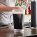 A man pours dark liquid into a Carlisle Clear Polycarbonate Beverage Pitcher.