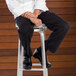 A man sitting on a stool wearing Uncommon Chef classic black chef pants.