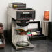 A Bunn pourover coffee maker on a counter with a glass coffee pot next to it.