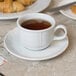 A bright white Tuxton china saucer with a cup of coffee on it.