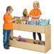 A boy and girl in orange and blue shirts standing next to a Young Time natural wooden bookshelf filled with books.