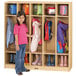A little girl standing in front of a Jonti-Craft coat locker with many coats hanging inside.