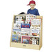 A young boy standing next to a wooden book display stand filled with books.