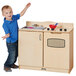 A young boy standing next to a wooden kitchen with a sink.