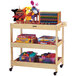 A Jonti-Craft wooden supply cart with toys on top.