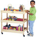 A young boy in a green shirt using a Jonti-Craft mobile wood supply cart to hold art supplies.