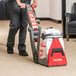 A person using a Sanitaire upright carpet extractor to clean a carpet.