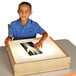 A young boy sitting at a table with a Jonti-Craft wood frame LED light box.