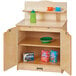 A Jonti-Craft wooden toddler kitchen cupboard with a green and yellow plate, a green bottle with a blue lid on it.