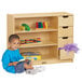 A young boy sitting on the floor next to a Jonti-Craft wood storage module with yellow drawers.