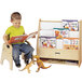 A young boy sitting in a chair reading a book on a Jonti-Craft wood book stand.