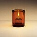 A Sterno amber mini bubbles glass candle holder with an orange candle lit inside.