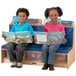 Children sitting on a Jonti-Craft wood bench with blue padded seating reading books.