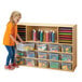 A girl standing next to a Young Time natural sectional cubbie storage unit with clear trays.