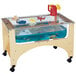 A Jonti-Craft mobile wooden sensory table with see-thru sides filled with water and toys.