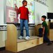 Two boys standing on a Jonti-Craft wooden storage step writing on a whiteboard.