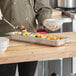 A person in a chef's uniform using a Vollrath stainless steel steam table pan to serve fruit.