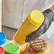 A person in black gloves using a Tablecraft yellow end cap to dispense mustard.