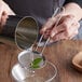 A person using a Tablecraft stainless steel fine mesh cocktail strainer to pour water into a glass.