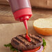 A Tablecraft red squeeze bottle cap pouring ketchup on a burger.