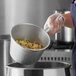A person in a white apron using a Vollrath aluminum dipper to pour food into a pot.
