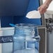 A person using an Avantco ice scoop to pour ice into a clear container.