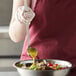 A woman using a Vollrath stainless steel ladle to pour dressing on a salad at a salad bar.