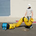 A man in a hard hat using a yellow and black tube with a blue XPOWER X-12 ventilator fan.