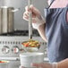 A woman using a Vollrath stainless steel ladle to pour liquid into a bowl of food.