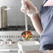 A woman in an apron using a Vollrath stainless steel ladle to serve soup over a white bowl.