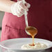 A person using a Vollrath stainless steel ladle to pour brown liquid on a plate of food.