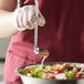 A person using a Vollrath stainless steel ladle to pour sauce over a bowl of salad.