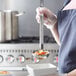 A woman using a Vollrath Jacob's Pride stainless steel ladle to serve soup into a white bowl.