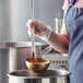 A person using a Vollrath stainless steel ladle to serve orange soup from a pot.