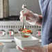 A person in a blue shirt using a Vollrath Jacob's Pride stainless steel ladle to serve soup.