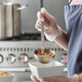 A person using a Vollrath stainless steel ladle to pour soup into a bowl.