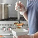 A person using a Vollrath Jacob's Pride stainless steel ladle to serve food from a bowl.