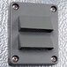 A grey rectangular Kolpak wall plate with two metal corners and two holes.