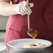 A person using a Vollrath stainless steel ladle to pour brown liquid on a plate.