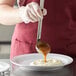 A person using a Vollrath stainless steel ladle to pour brown liquid onto a plate of food.