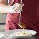 A person using a Vollrath stainless steel ladle to pour sauce over mashed potatoes.