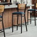 Three Lancaster Table & Seating bar stools with blue vinyl seats and natural wood backs next to a counter.