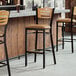 Three Lancaster Table & Seating restaurant bar stools with natural wood backs and light brown vinyl seats.